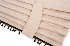 Beige Alkantara-Optik Durchschlupfgardine mit dunkler Quastenborte und Halteband, gefaltet.