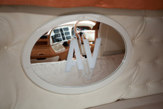 Ovaler LKW-Spiegel mit wei�em Rahmen und sandgestrahltem "AV"-Motiv, eingebaut in eine beige LKW-Kabine.