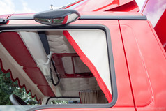 Wei�er Polyester-Gardinenschal mit rotem Fransensaum, im Fenster eines roten LKW-Fahrerhauses montiert.