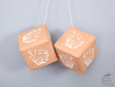 Beigefarbene Kunstleder-W�rfel mit wei�em L�wenkopf-Stick, als Paar an Schn�ren h�ngend.