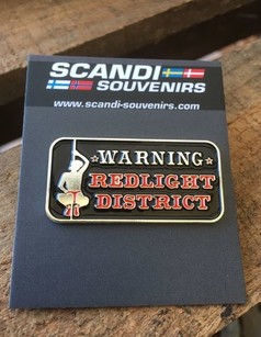 Ein schwarzer Scandi Pin aus Metall mit silbernem Rand, roter Schrift "WARNING REDLIGHT DISTRICT" und silberner Figur an einer Stange.