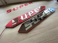 Beleuchteter SUPER Schriftzug aus spiegelpoliertem Edelstahl auf roten und schwarzen Platten.