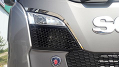 Gl�nzende Chrom-B�gen um den Scheinwerfer eines grauen Scania NG LKWs mit Scania Logo.