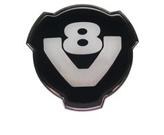 DG K�hleremblem V8 aus schwarzem Plastik mit wei�em V8-Schriftzug und Chromrand.