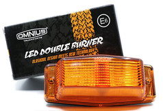 Orangefarbene Omnius LED Double Burner Lampe mit gerippter PC-Linse. Dahinter die schwarze Verpackung mit 